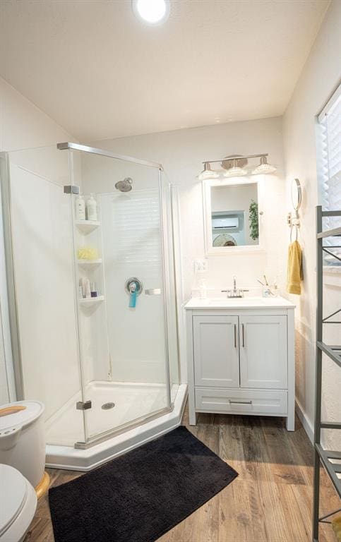 bathroom with wood-type flooring, vanity, toilet, and a shower with shower door