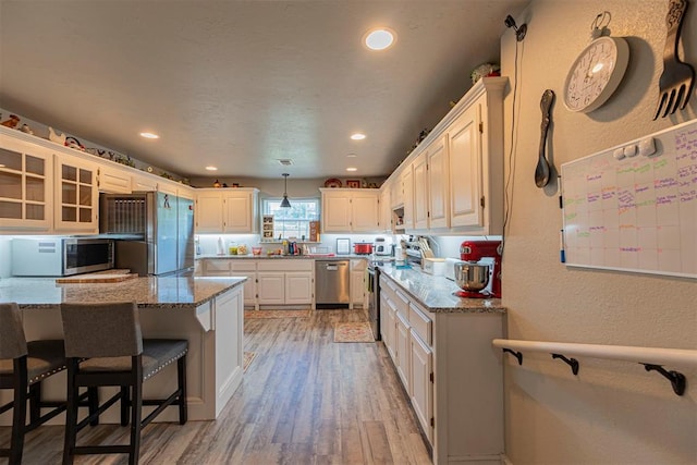 kitchen with white cabinets, appliances with stainless steel finishes, light hardwood / wood-style floors, and light stone countertops