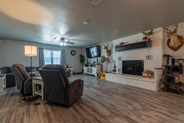 living room with a textured ceiling, ceiling fan, a wood stove, and dark wood-type flooring