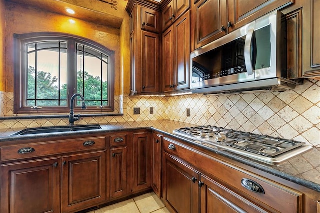 kitchen with sink, backsplash, dark stone countertops, light tile patterned floors, and appliances with stainless steel finishes