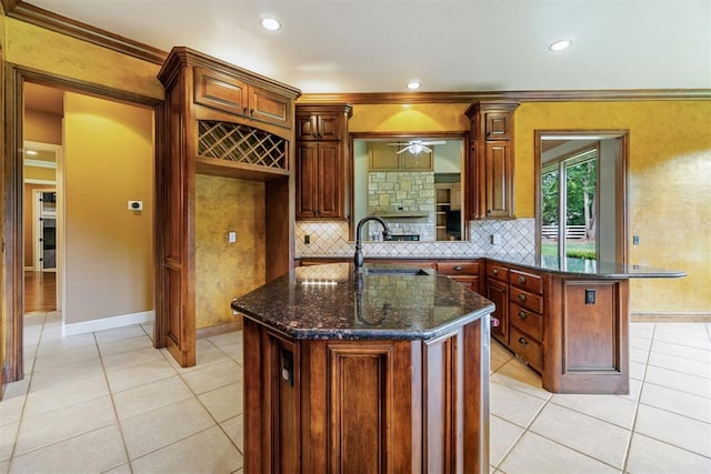 kitchen with ornamental molding, sink, light tile patterned floors, dark stone countertops, and a center island