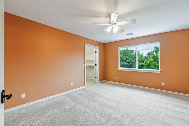 unfurnished bedroom with light carpet, a closet, a spacious closet, and ceiling fan