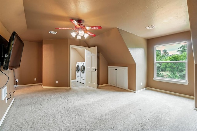 additional living space with washing machine and clothes dryer, ceiling fan, light colored carpet, and vaulted ceiling