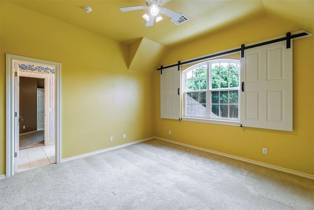 unfurnished room featuring light carpet, a barn door, vaulted ceiling, and ceiling fan