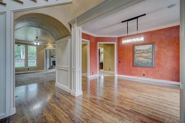 spare room with ornate columns, ornamental molding, wood finished floors, and a ceiling fan