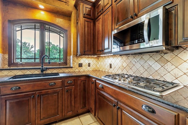 kitchen featuring dark countertops, tasteful backsplash, appliances with stainless steel finishes, a sink, and light tile patterned floors