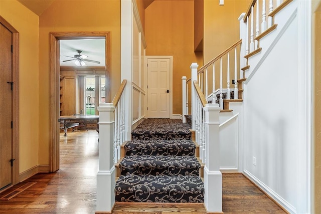 stairs featuring a ceiling fan, a towering ceiling, baseboards, and wood finished floors