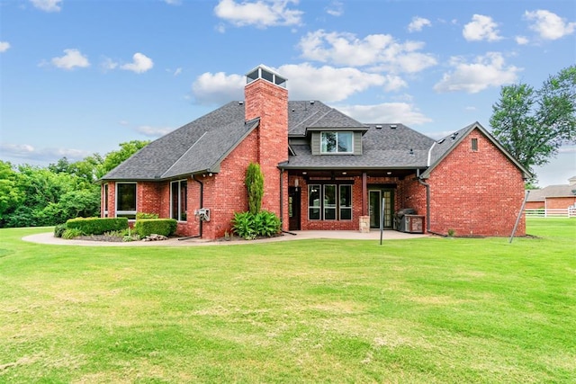back of property with brick siding, roof with shingles, a yard, and a patio area