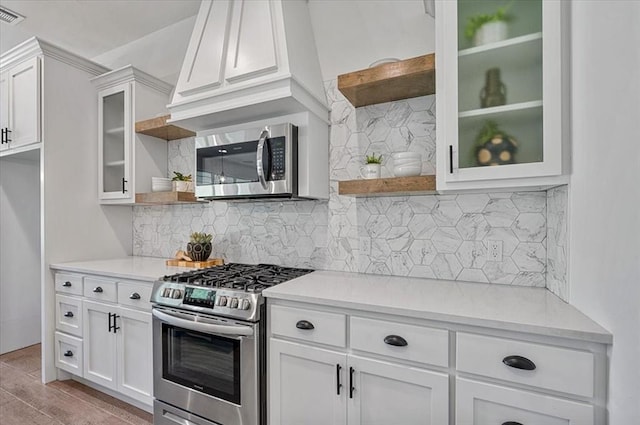 kitchen featuring tasteful backsplash, white cabinetry, light wood-type flooring, and appliances with stainless steel finishes