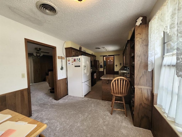 kitchen featuring white refrigerator with ice dispenser, carpet, a healthy amount of sunlight, and wood walls