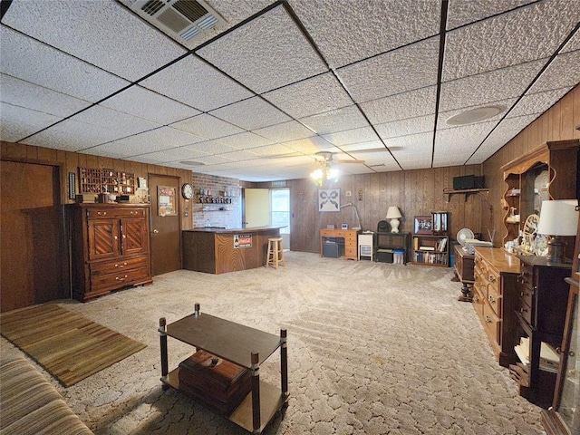 living room with carpet, a drop ceiling, ceiling fan, and wood walls