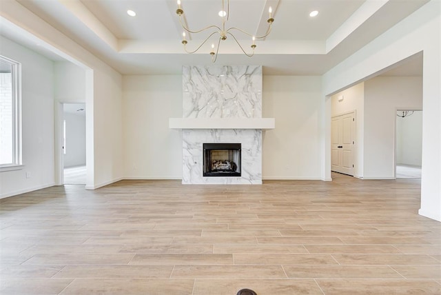 unfurnished living room featuring a fireplace, light wood-type flooring, and a raised ceiling