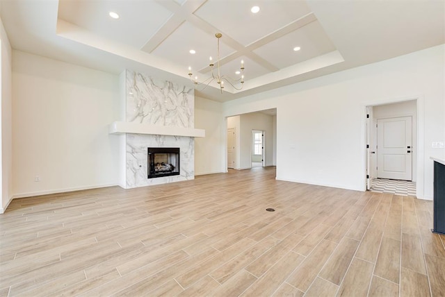 unfurnished living room with a fireplace, light hardwood / wood-style flooring, coffered ceiling, and a notable chandelier