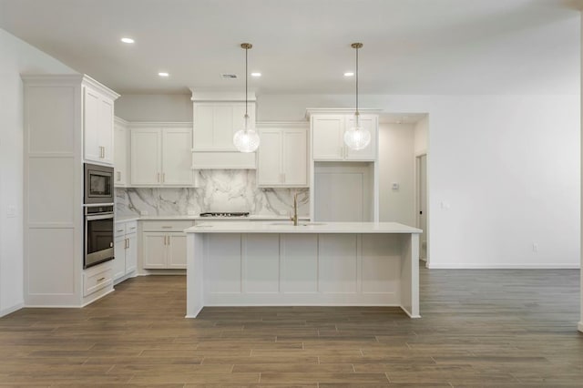 kitchen with white cabinets, stainless steel appliances, hanging light fixtures, and an island with sink