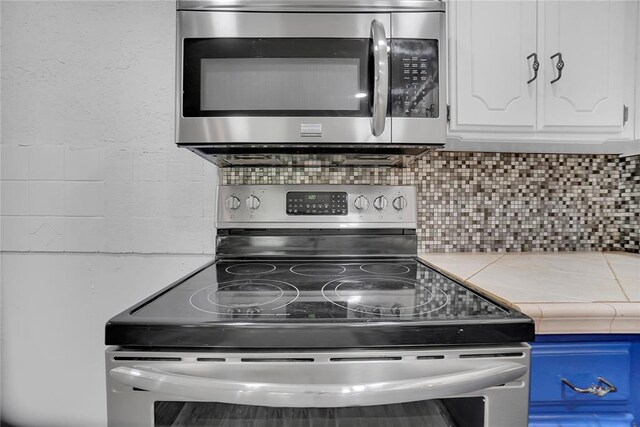 kitchen with tile countertops, decorative backsplash, white cabinets, and stainless steel appliances