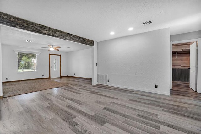 unfurnished room with ceiling fan, light hardwood / wood-style flooring, beamed ceiling, and a textured ceiling