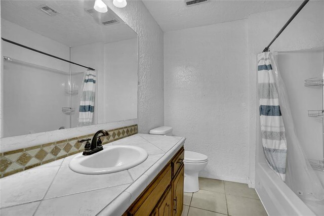 full bathroom with a textured ceiling, vanity, shower / bath combo with shower curtain, tile patterned flooring, and toilet