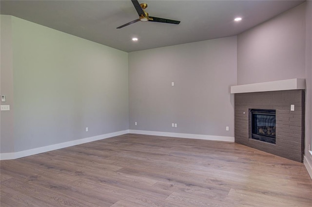 unfurnished living room with a brick fireplace, light hardwood / wood-style flooring, and ceiling fan