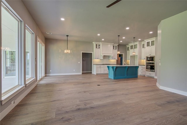 kitchen with light hardwood / wood-style flooring, pendant lighting, a kitchen island with sink, white cabinets, and appliances with stainless steel finishes