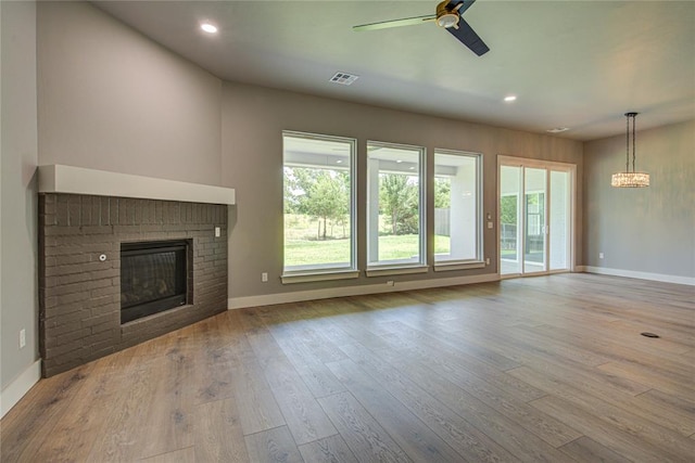 unfurnished living room featuring a brick fireplace, ceiling fan with notable chandelier, and light wood-type flooring