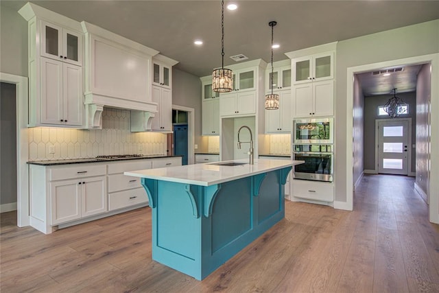 kitchen featuring sink, light hardwood / wood-style flooring, an island with sink, decorative light fixtures, and a kitchen bar