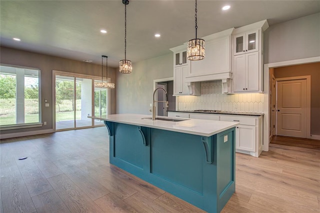 kitchen with white cabinetry, sink, an island with sink, light hardwood / wood-style floors, and decorative light fixtures