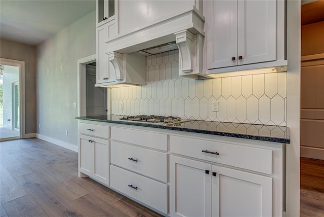 kitchen featuring decorative backsplash, light hardwood / wood-style flooring, dark stone countertops, white cabinets, and stainless steel gas stovetop