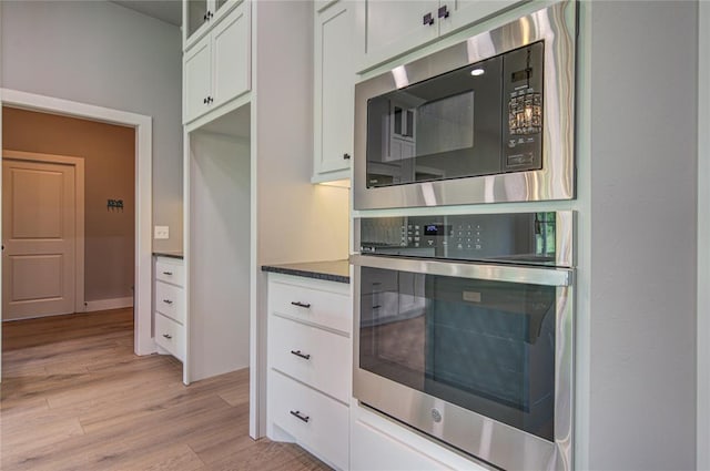 kitchen with appliances with stainless steel finishes, light hardwood / wood-style flooring, white cabinetry, and dark stone counters