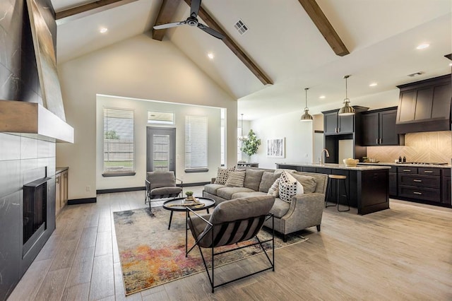 living room with sink, beamed ceiling, high vaulted ceiling, light hardwood / wood-style floors, and a fireplace