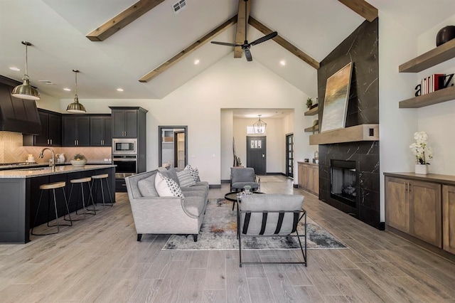 living room with a fireplace, beamed ceiling, high vaulted ceiling, and light wood-type flooring