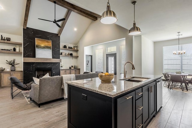 kitchen with light stone countertops, light wood-type flooring, a kitchen island with sink, and sink