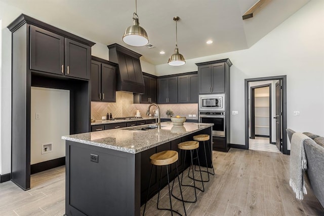 kitchen with light stone countertops, sink, an island with sink, light hardwood / wood-style floors, and appliances with stainless steel finishes