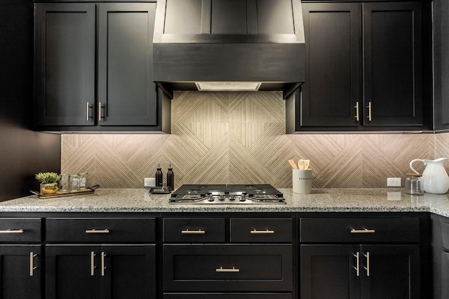 kitchen featuring stainless steel gas cooktop, light stone countertops, backsplash, and range hood