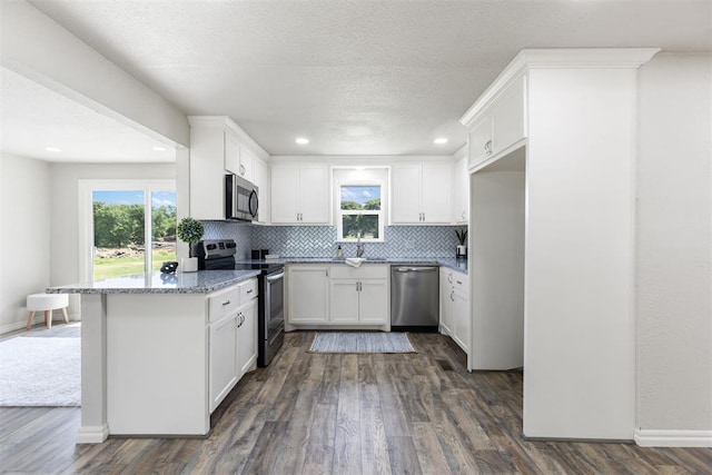 kitchen with white cabinetry, dark wood-type flooring, stainless steel appliances, light stone counters, and backsplash