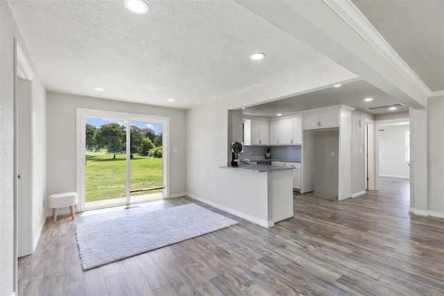 kitchen with kitchen peninsula, hardwood / wood-style flooring, decorative backsplash, a textured ceiling, and white cabinetry