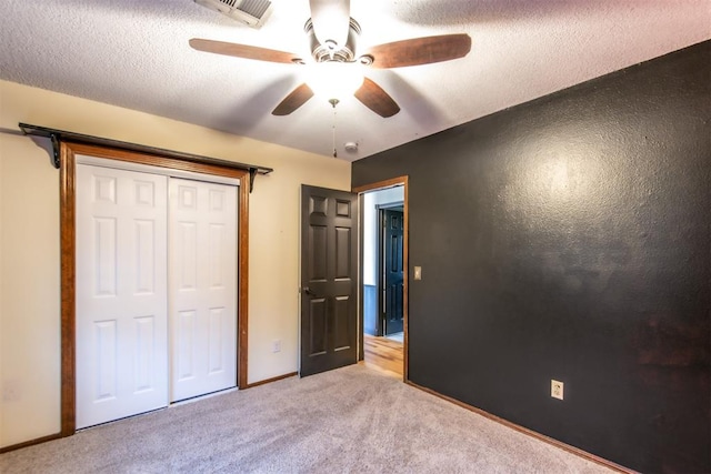 unfurnished bedroom featuring ceiling fan, a closet, light carpet, and a textured ceiling