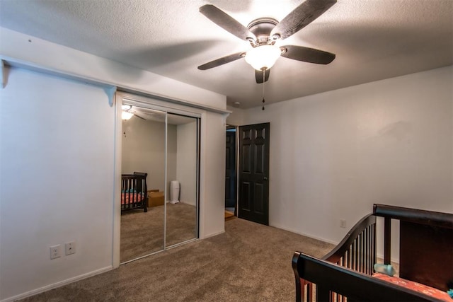 carpeted bedroom featuring ceiling fan, a closet, a textured ceiling, and a nursery area