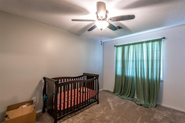 bedroom with a textured ceiling, a nursery area, carpet floors, and ceiling fan