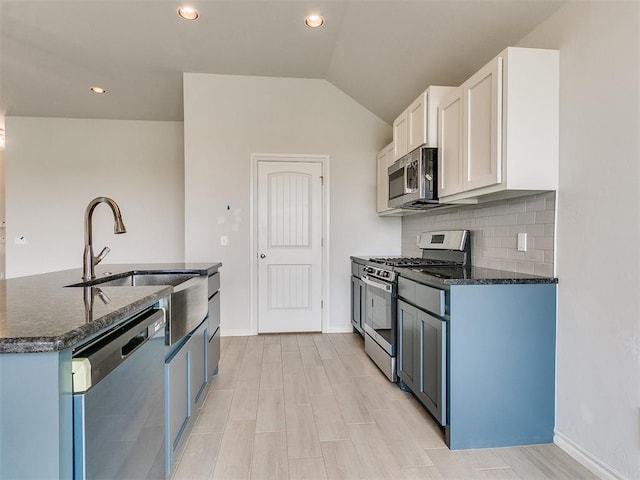 kitchen with blue cabinetry, white cabinetry, dark stone counters, vaulted ceiling, and appliances with stainless steel finishes