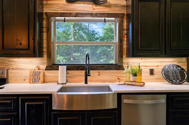 kitchen featuring dishwasher, sink, wood walls, and plenty of natural light