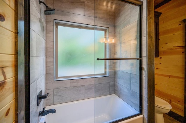 bathroom with shower / bath combination with glass door, toilet, and wooden walls