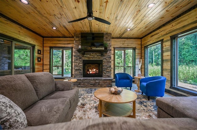 living room with plenty of natural light, ceiling fan, a stone fireplace, and wood ceiling