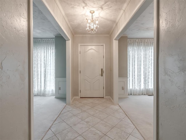 foyer entrance featuring an inviting chandelier, ornamental molding, a textured wall, and light colored carpet