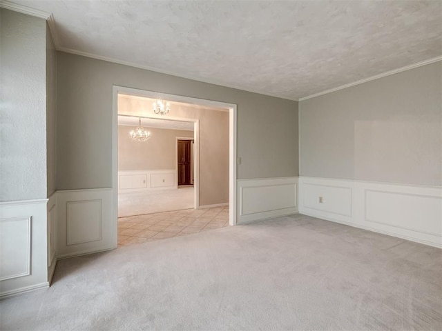 carpeted spare room with ornamental molding, wainscoting, a decorative wall, and a notable chandelier