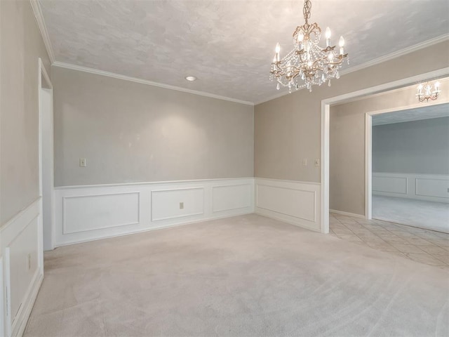 carpeted empty room featuring wainscoting, ornamental molding, a decorative wall, and a chandelier
