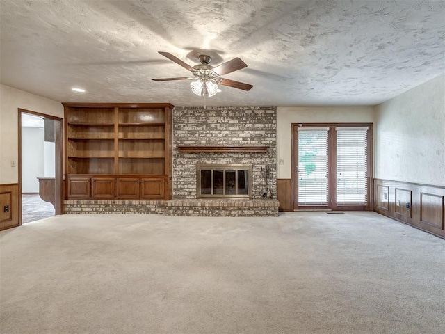 unfurnished living room featuring wainscoting, carpet, a ceiling fan, and a brick fireplace