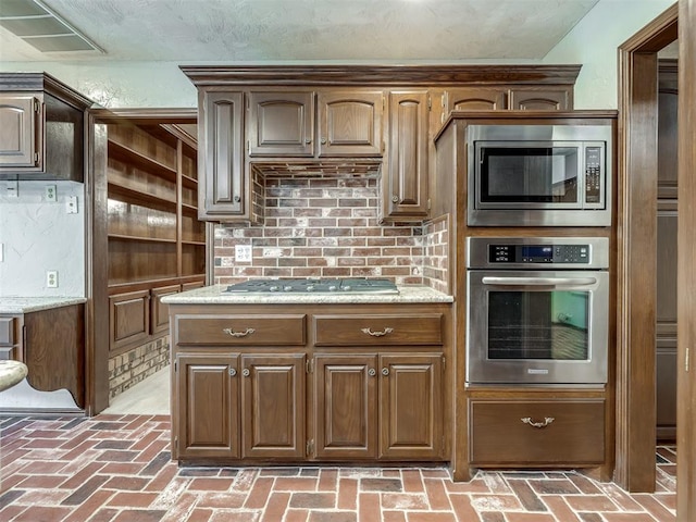 kitchen with backsplash, appliances with stainless steel finishes, and brick floor