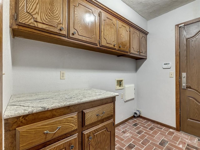 clothes washing area with washer hookup, baseboards, cabinet space, and brick floor