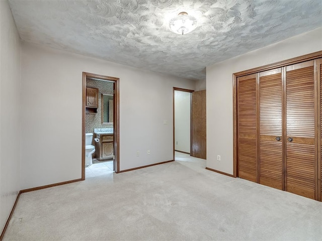 unfurnished bedroom with a closet, baseboards, ensuite bath, and light colored carpet