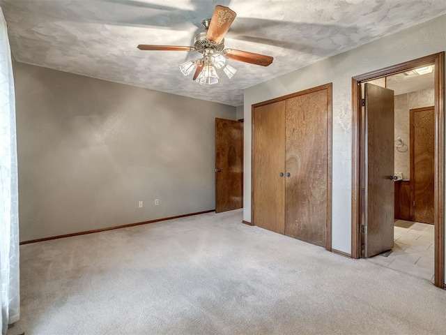 unfurnished bedroom featuring light colored carpet, a textured ceiling, baseboards, and ceiling fan